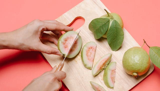 Crop woman cutting guavas on board