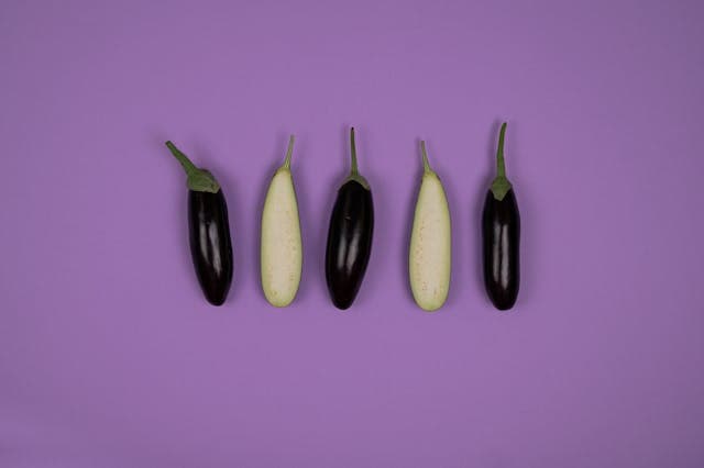 Whole and cut eggplants on purple background