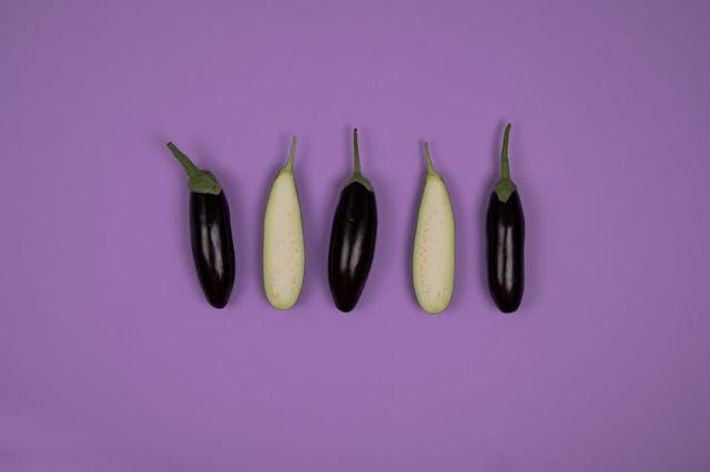 Whole and cut eggplants on purple background