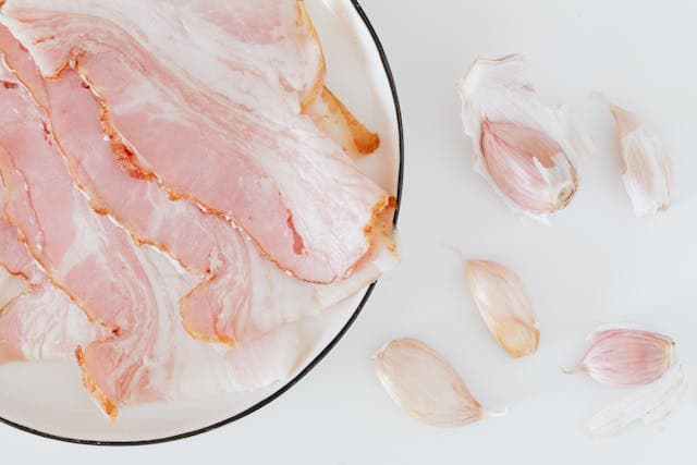 Composition of raw bacon and garlic on desk