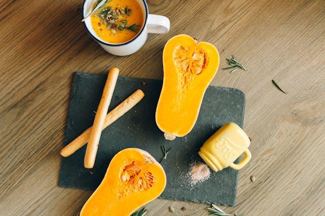 Cut Butternut Squash and Breadsticks Next to a Mug of Pumpkin Soup